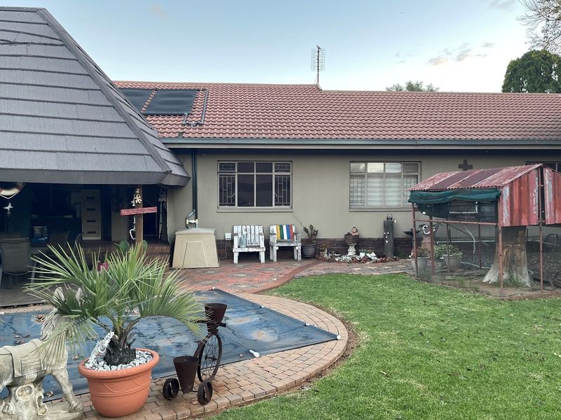 Rear view of the property featuring a paved patio area, a swimming pool with cover, and a garden space with a small outdoor structure.