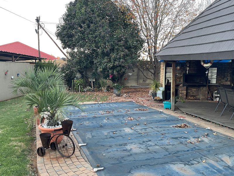Outdoor pool area featuring a covered swimming pool, adjacent brick-built braai area, and a paved patio space within a private garden setting.