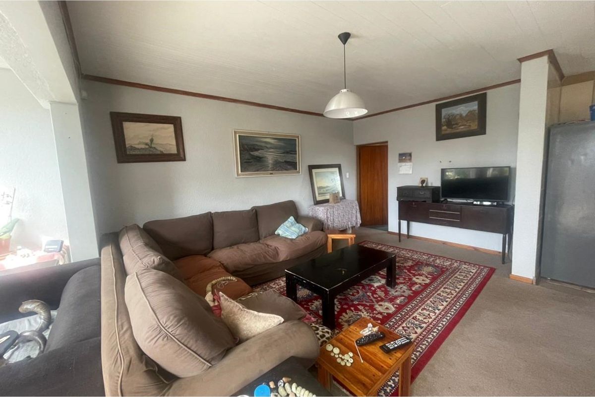 A living room featuring carpet flooring, a central pendant light fixture, and a wooden door leading to an adjacent area.