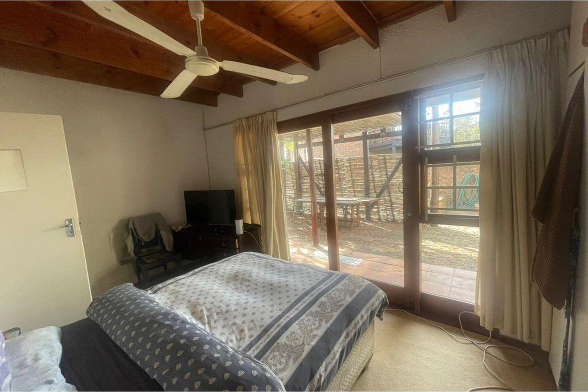A bedroom featuring exposed timber ceiling beams, a ceiling fan, and sliding glass doors providing direct access to an outdoor patio area.