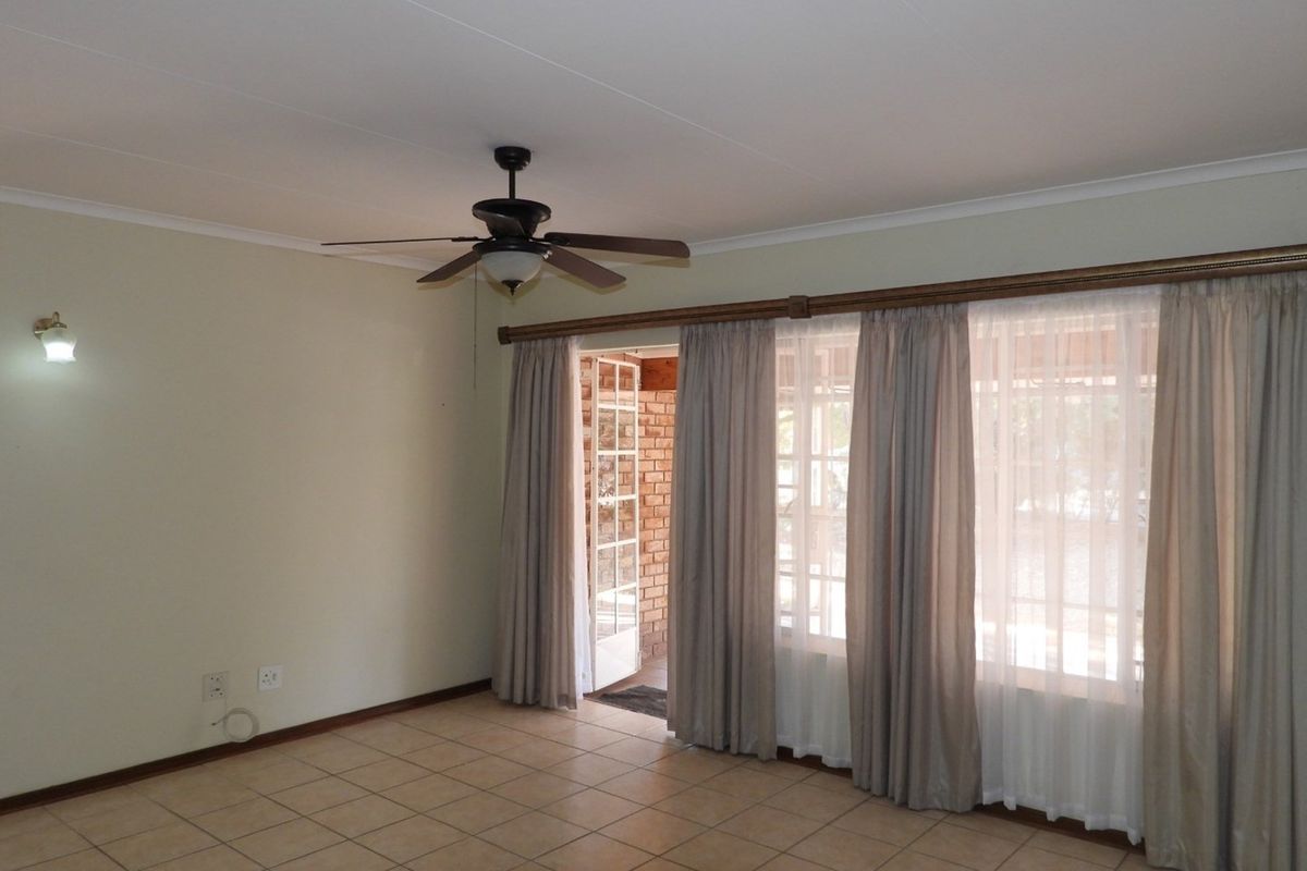 A spacious living room featuring tiled flooring, a ceiling fan, and large glass sliding doors providing access to an outdoor patio area.