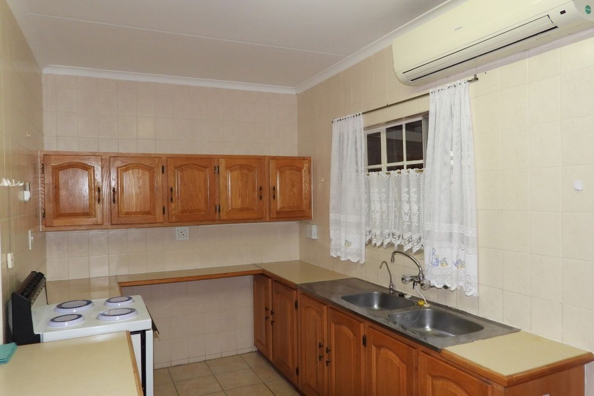 A functional kitchen featuring wooden cabinetry, tiled walls, a double basin sink, and a wall-mounted air conditioning unit.