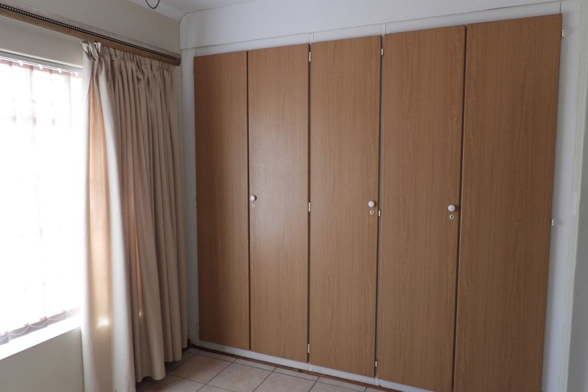 A bedroom featuring built-in wooden wardrobes and tiled flooring, providing ample storage space and natural light from the adjacent window.