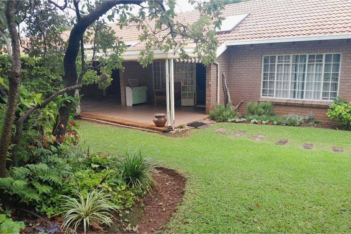 A rear view of the townhouse featuring a covered patio area, brick facade, tiled roof, and a well-maintained garden with established landscaping.