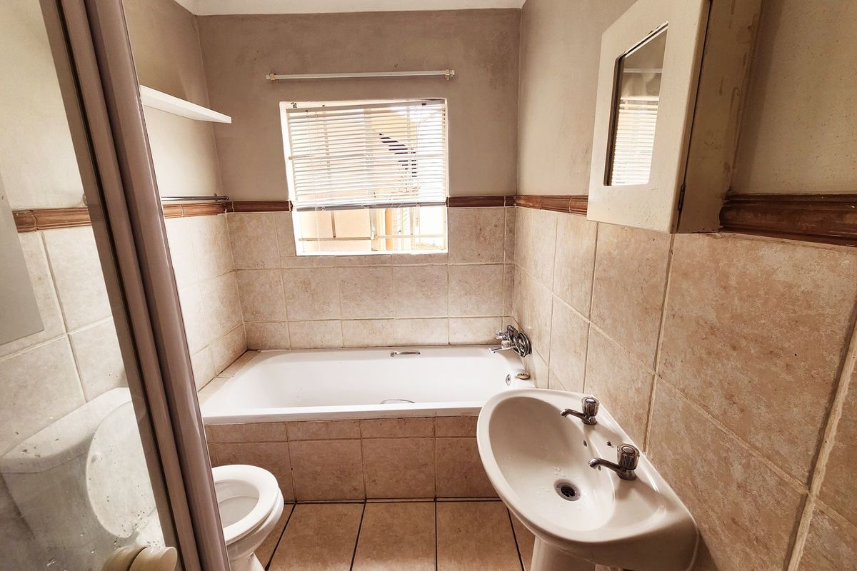 A functional bathroom featuring a bathtub, pedestal basin, toilet, and neutral tiled finishes, offering a practical layout with natural light from the window.