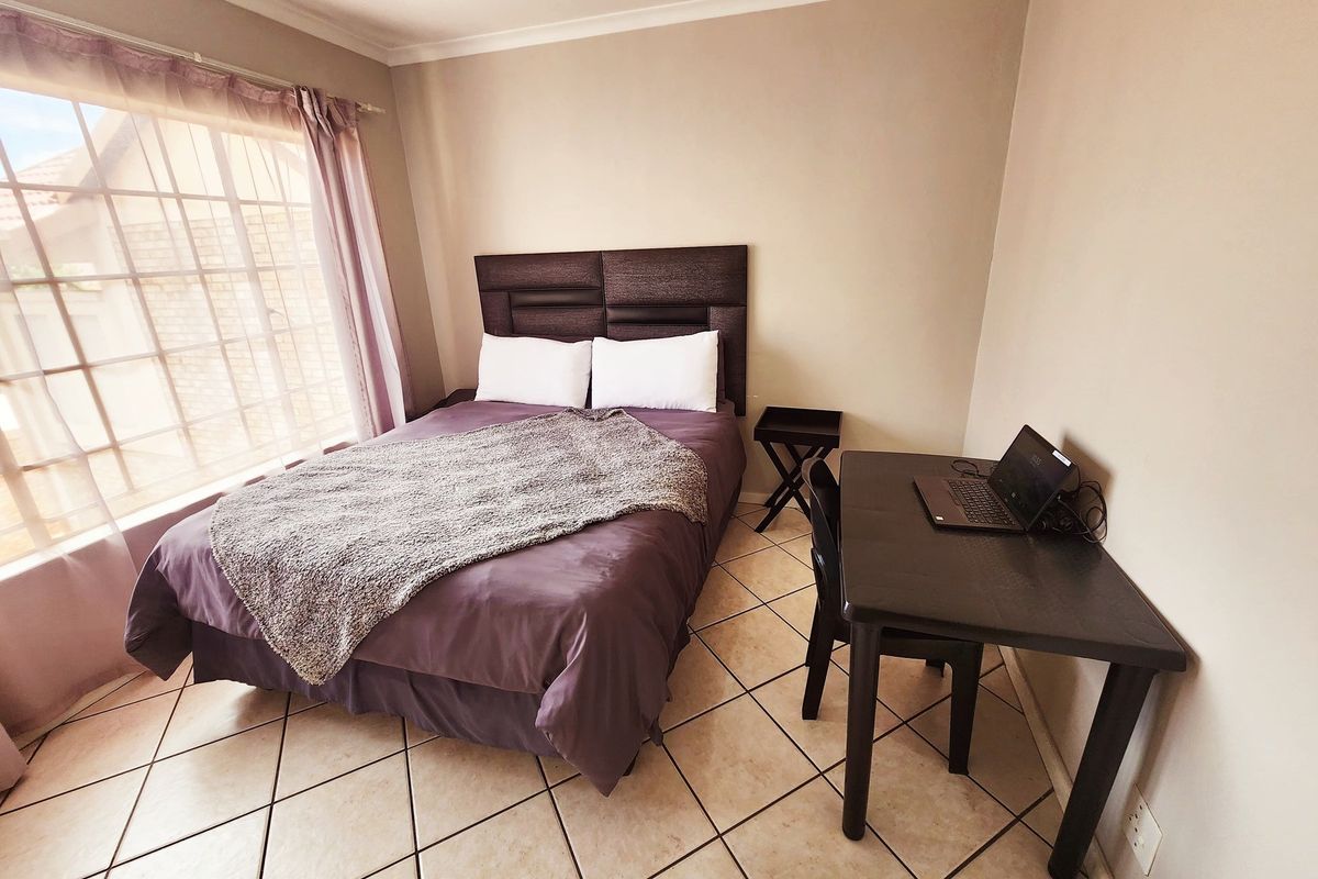 A functional bedroom featuring tiled flooring, a large window allowing natural light, and neutral wall finishes.