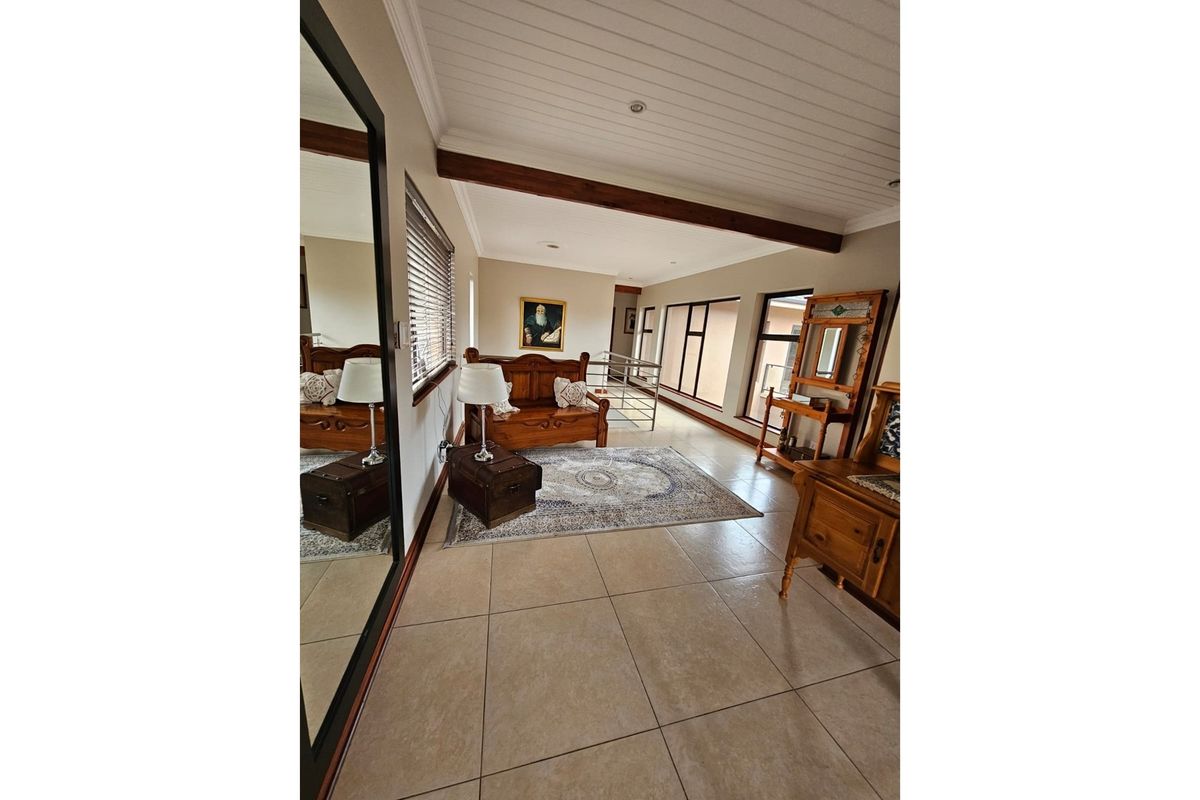 A spacious living area featuring tiled flooring, a white timber-paneled ceiling with exposed wooden beams, and large windows providing natural light.