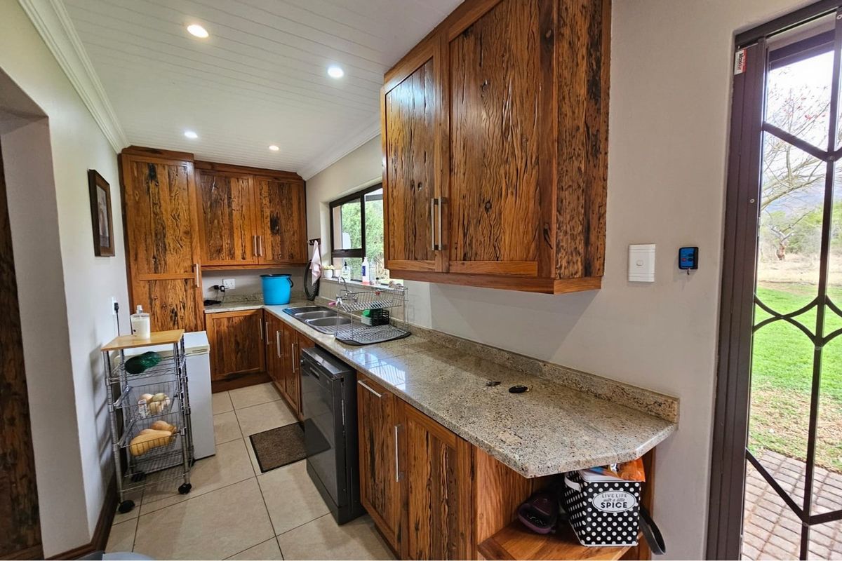 A functional kitchen featuring rustic timber cabinetry, granite countertops, a double sink, and tiled flooring with direct access to the outdoor area.
