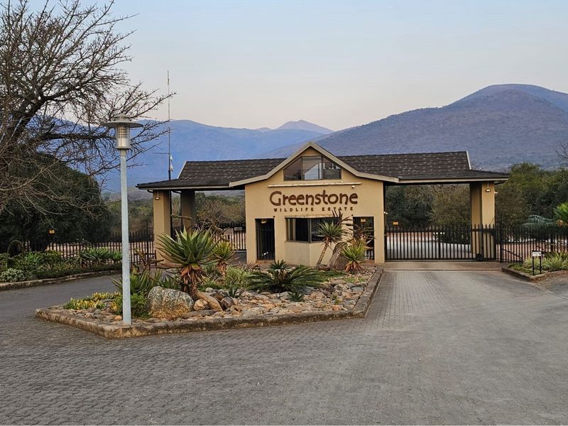 The secure entrance gatehouse of Greenstone Wildlife Estate, featuring paved driveway access, landscaped garden beds, and mountain views in the background.