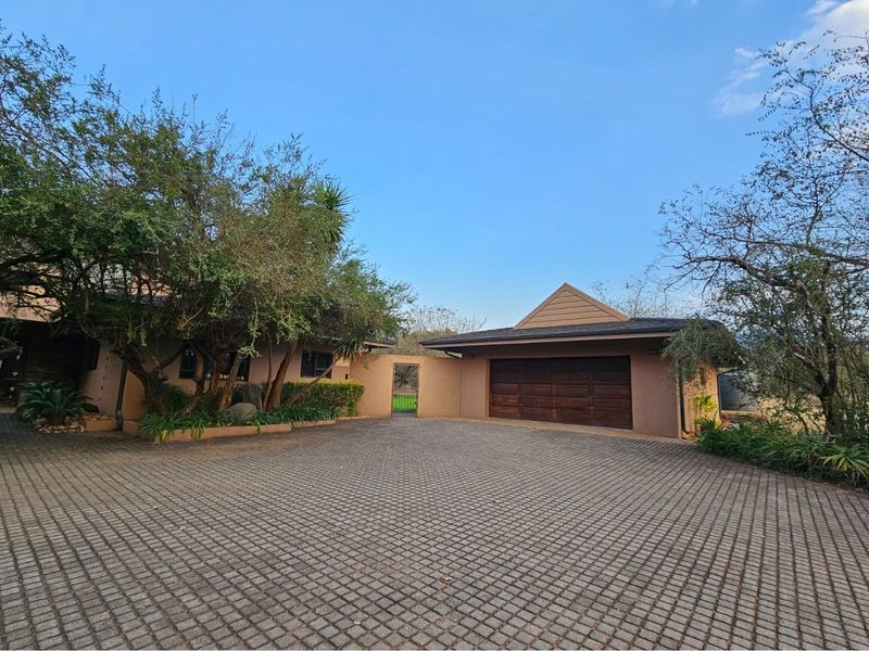 A spacious paved driveway leading to a double garage, featuring mature trees and established landscaping in a quiet residential setting.