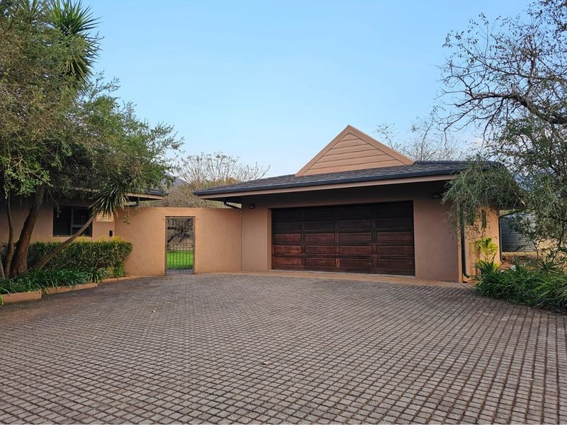 A well-maintained exterior front view featuring a paved driveway, a double garage with wooden doors, and a gated side entrance.