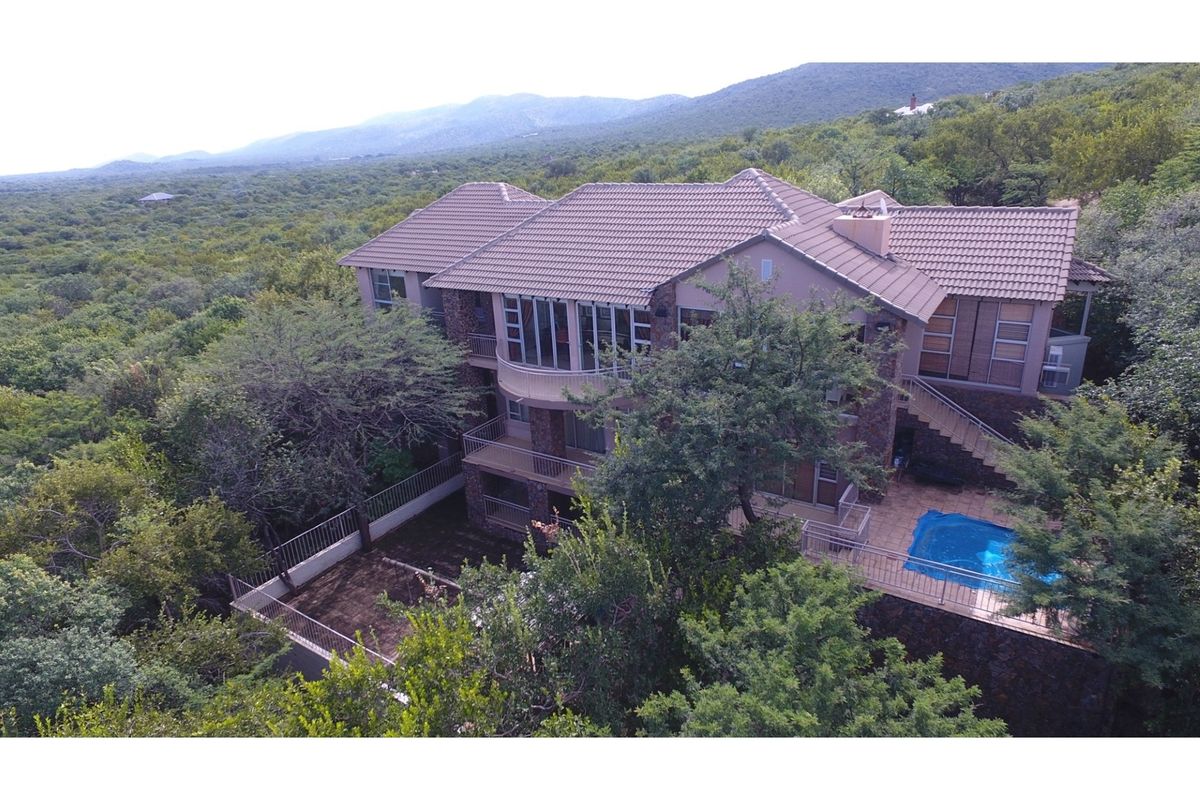 Aerial view of a multi-level residential property featuring stone cladding, tiled roofing, multiple balconies, and a private swimming pool set in a natural landscape.