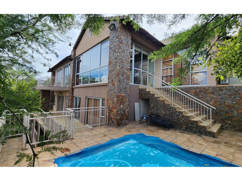 Rear exterior view of a multi-level house featuring stone cladding, a swimming pool with a patio, and large glass windows.