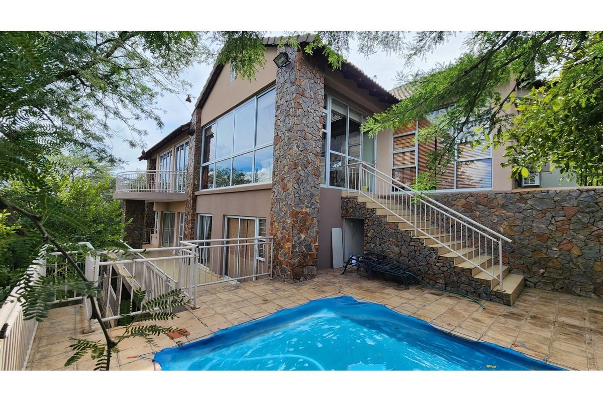 Rear exterior view of a multi-level house featuring stone cladding, a swimming pool with a patio, and large glass windows.
