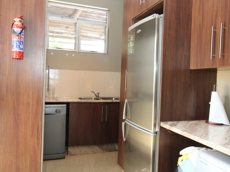 A functional scullery featuring dark wood cabinetry, granite countertops, a double basin sink, and tiled flooring, providing additional prep and wash-up space.