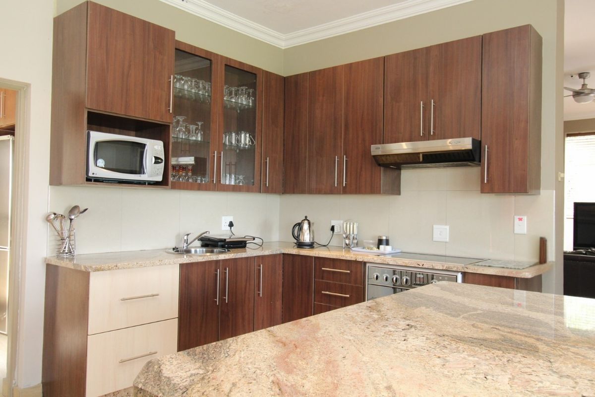 A functional kitchen featuring granite countertops, dark wood-finish cabinetry, built-in oven, extractor fan, and a convenient breakfast bar area.