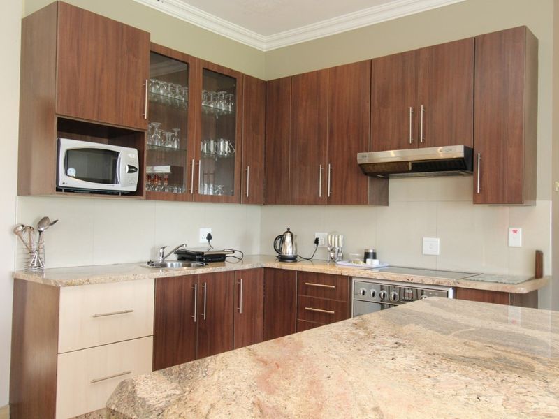 A functional kitchen featuring granite countertops, dark wood-finish cabinetry, built-in oven, extractor fan, and a convenient breakfast bar area.