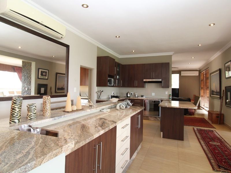 Spacious open-plan kitchen featuring dark wood cabinetry, granite countertops, integrated appliances, and recessed lighting, seamlessly flowing into the adjacent living area.