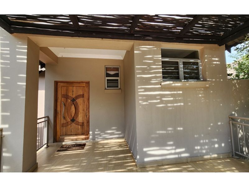 A covered patio area featuring tiled flooring, a timber pergola, and a decorative wooden entrance door with metal balustrades.