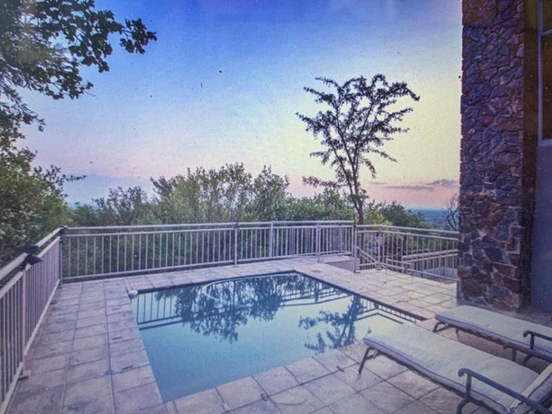 An elevated outdoor pool area featuring stone wall cladding, tiled decking, and metal safety railings with scenic views.