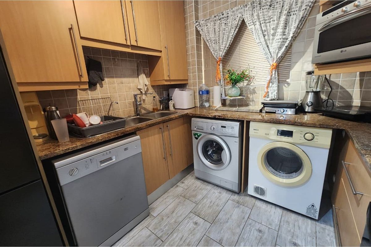 Compact kitchen featuring light wood cabinetry, granite-effect countertops, tiled backsplash, and integrated laundry appliances.