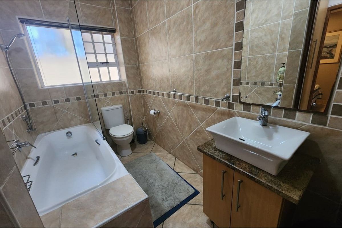 A functional bathroom featuring a built-in bathtub with glass screen, a vessel sink vanity, and full-height wall tiling.