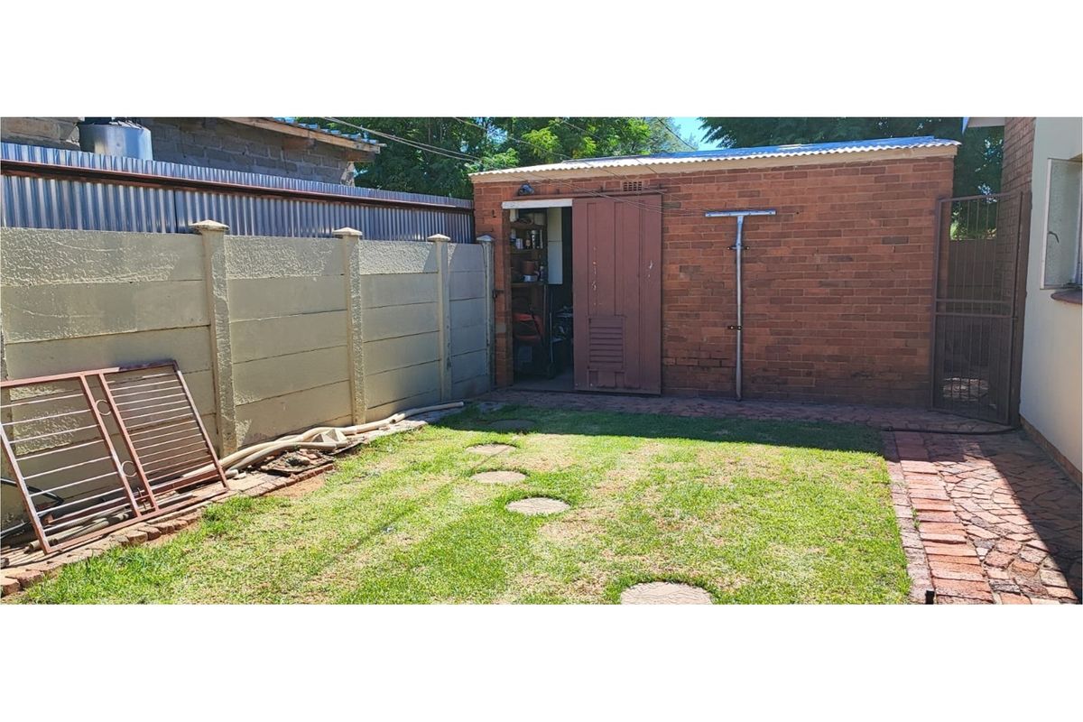 A rear garden area featuring a brick outbuilding with a sliding door, concrete boundary wall, and paved walkway.