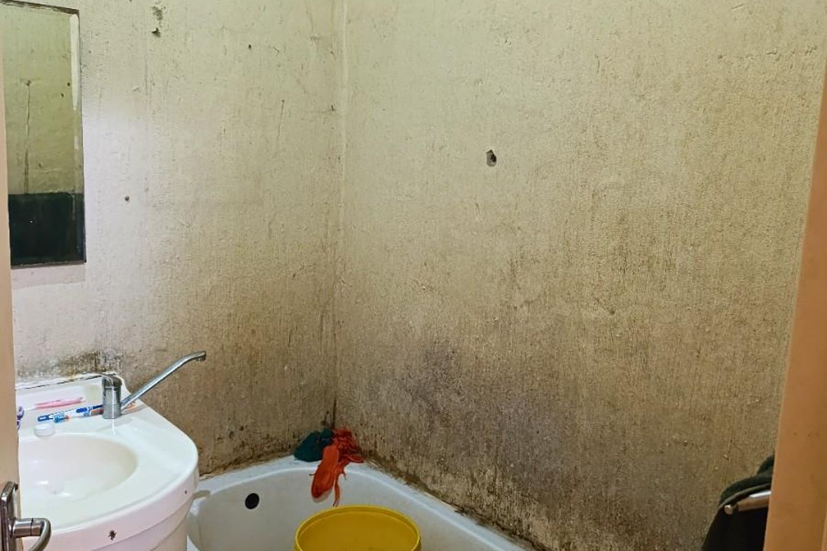 A small bathroom featuring a bathtub and pedestal basin, currently requiring significant renovation and repair to the wall finishes and fixtures.