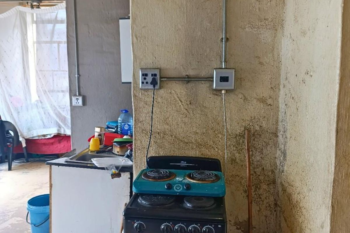 A basic kitchen area featuring a freestanding stove, exposed electrical conduit, and unfinished wall surfaces in need of renovation.