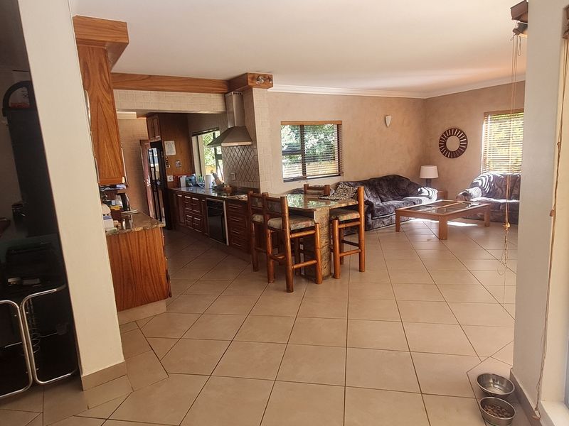 Spacious open-plan living area featuring a kitchen with granite countertops, wooden cabinetry, and tiled flooring throughout, seamlessly connecting to the lounge space.