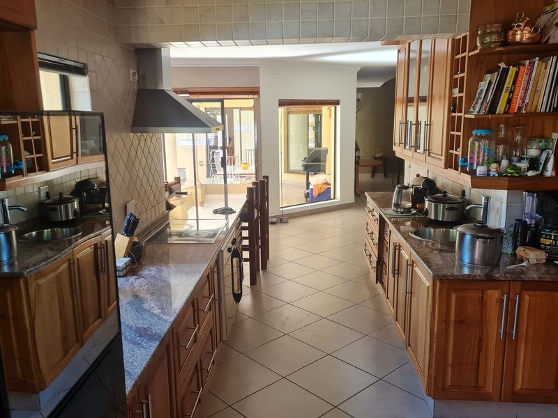 A functional galley-style kitchen featuring wooden cabinetry, granite countertops, tiled backsplash, and integrated appliances, leading through to an adjacent living area.