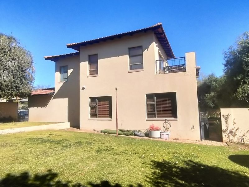Rear view of a double-story house featuring a tiled roof, upper-level balcony with metal railing, and a private garden area.