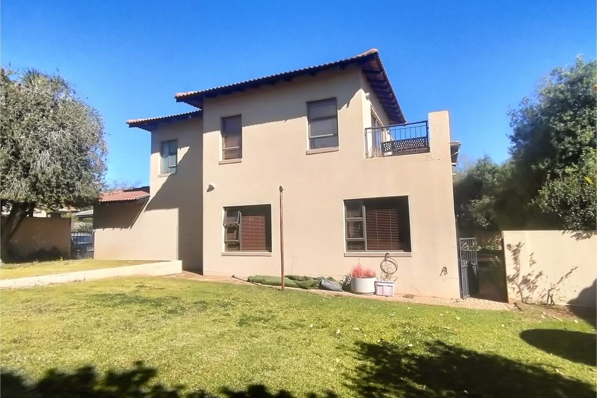 Rear view of a double-story house featuring a tiled roof, upper-level balcony with metal railing, and a private garden area.