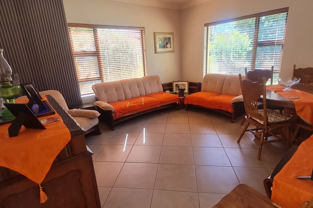 A spacious living area featuring neutral tiled flooring, coved cornicing, and large windows fitted with venetian blinds, offering a bright and functional living space.