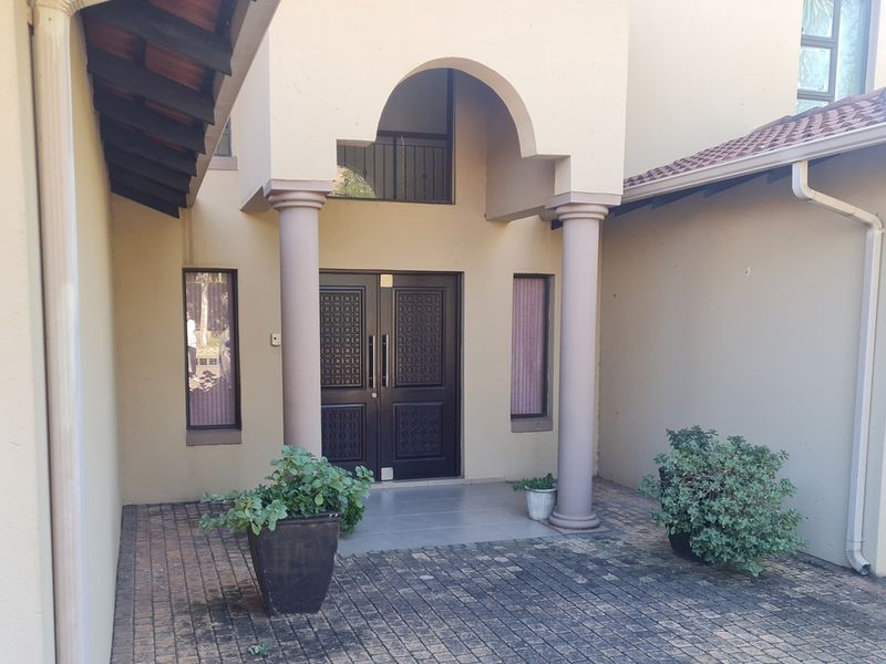 The front entrance features a covered portico with columns and a double door, leading to a paved driveway area.