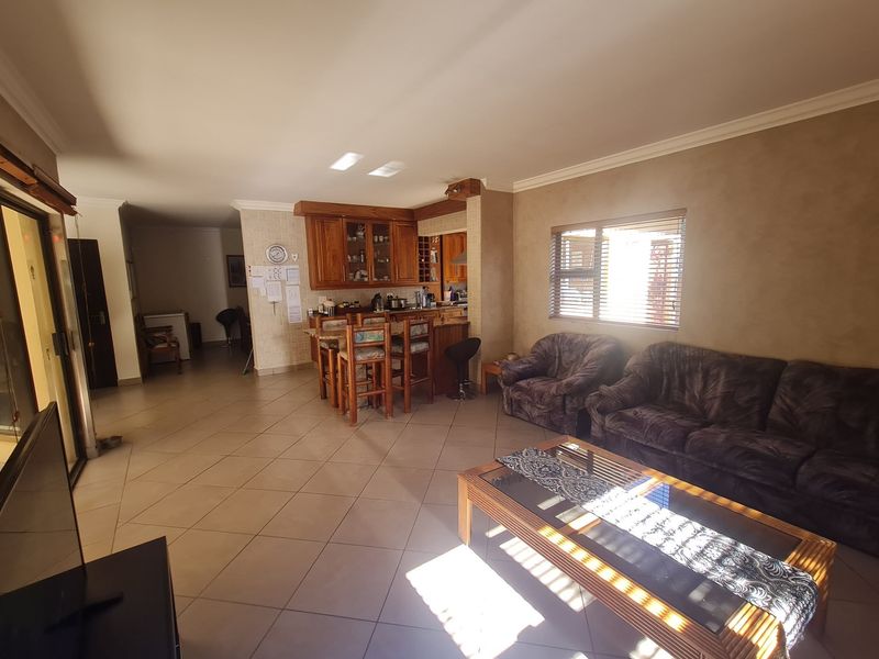 Spacious open-plan living area featuring tiled flooring, a wooden kitchen with a breakfast bar, and natural light through sliding glass doors.