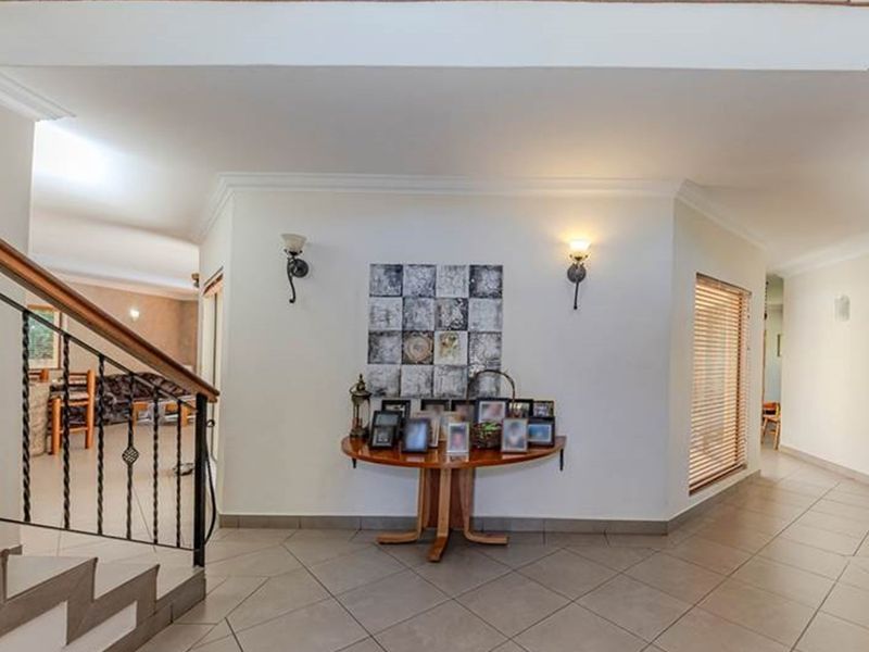 Spacious entrance hall featuring tiled flooring, a staircase with a decorative wrought iron balustrade, and wall-mounted lighting fixtures.
