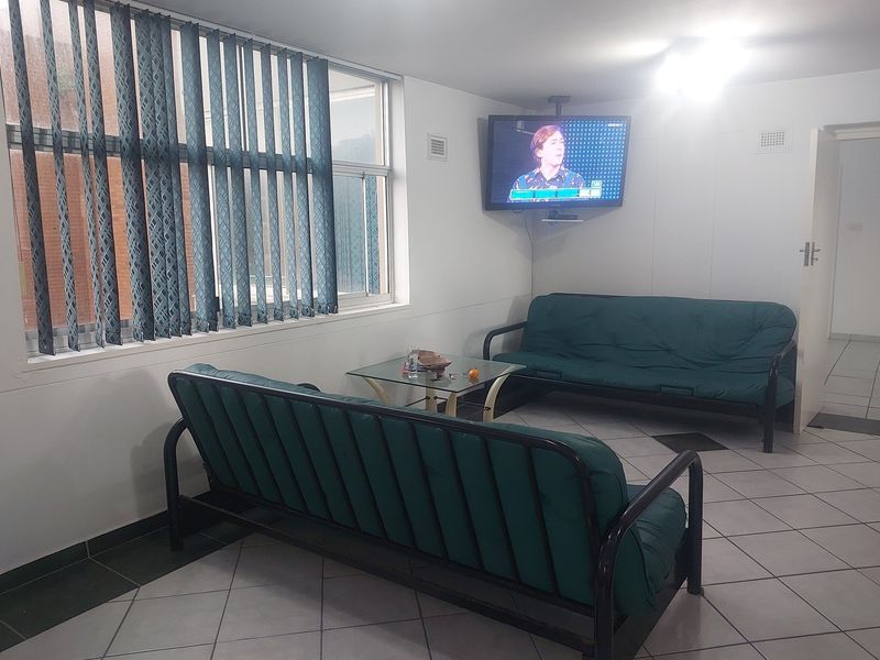 A functional living room area featuring tiled flooring, vertical window blinds, and a wall-mounted television bracket.