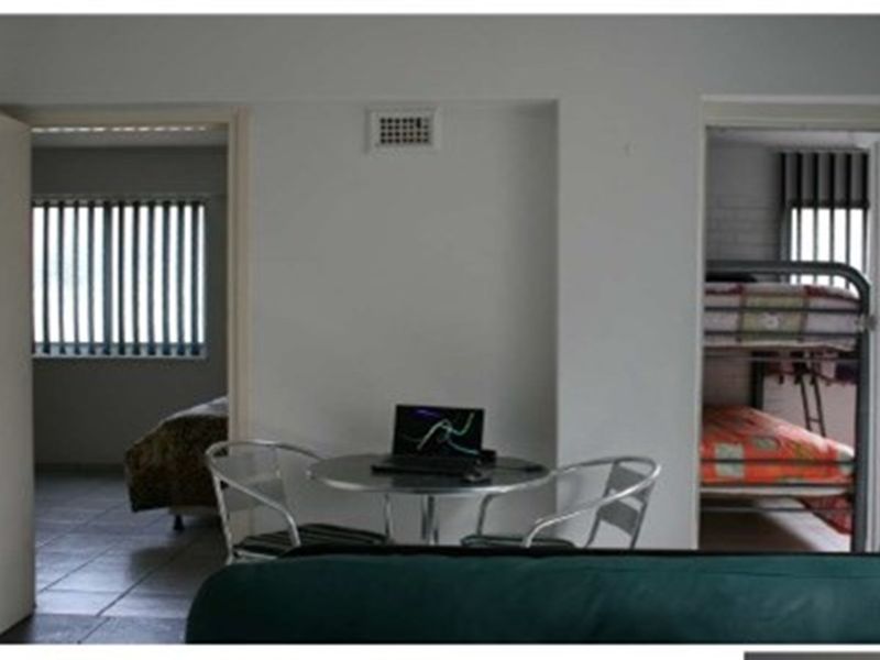 A view looking through a central living area into two adjacent bedrooms, featuring tiled flooring and vertical window blinds.