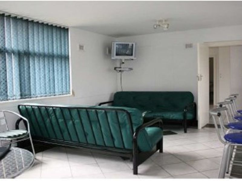 A dated living area featuring tiled flooring, vertical window blinds, and a wall-mounted television setup.