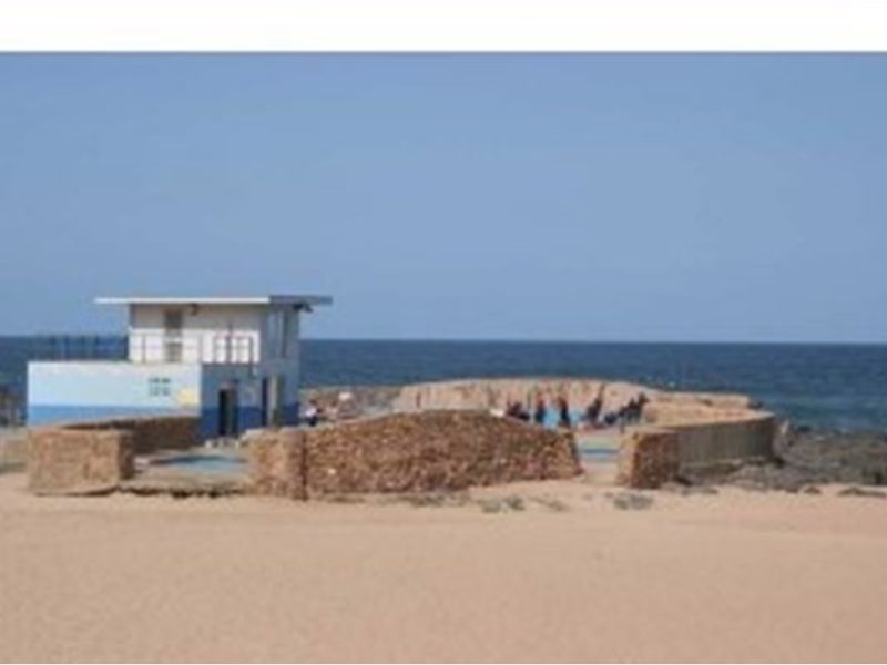 A coastal pool area featuring a small utility structure and a stone perimeter wall, situated directly on the beach with ocean views.