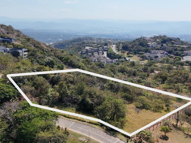 An aerial view of a vacant residential plot featuring sloped terrain and native vegetation, situated within a scenic hillside estate.