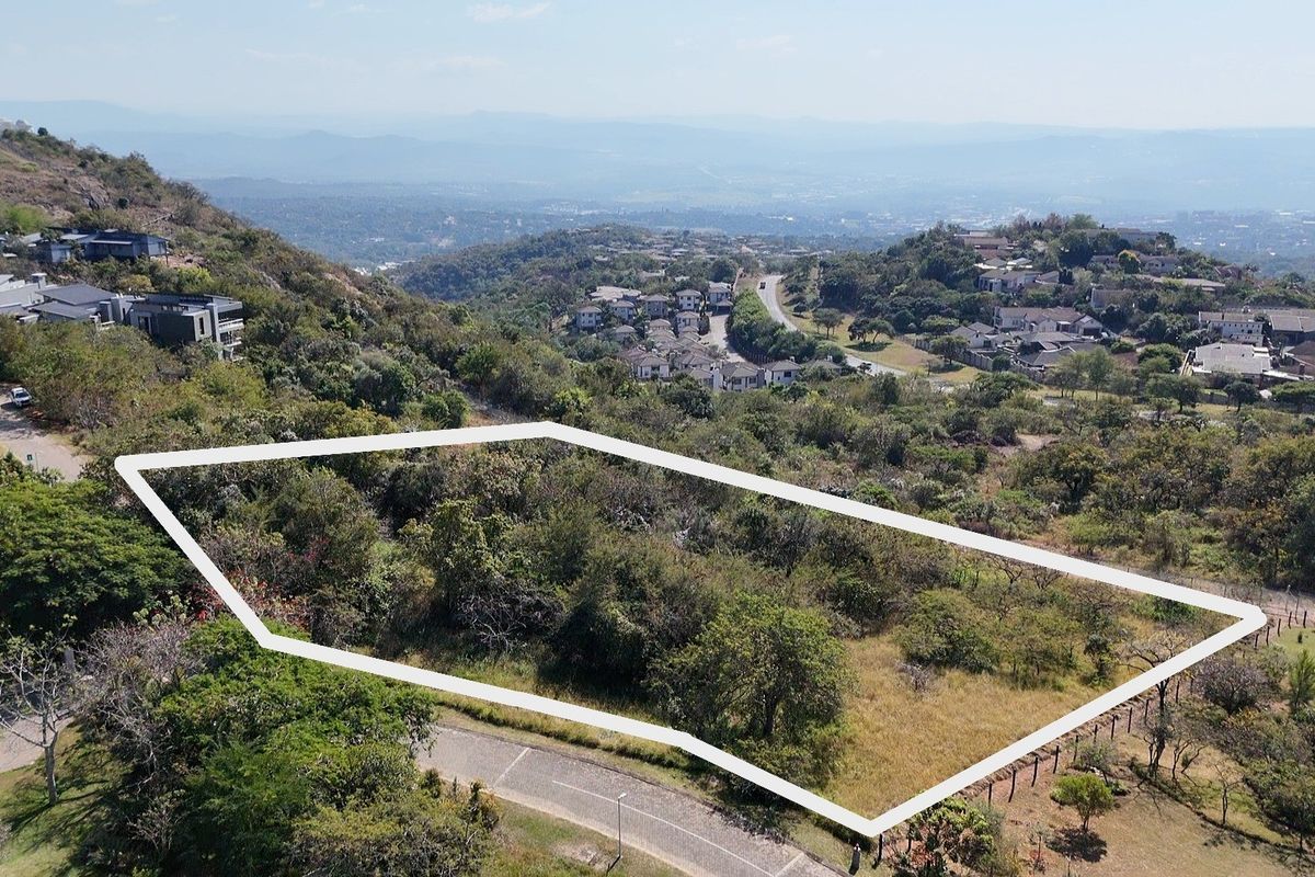 An aerial view of a vacant residential plot featuring sloped terrain and native vegetation, situated within a scenic hillside estate.