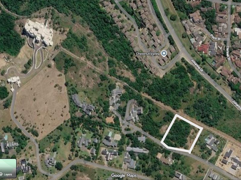 An aerial view of a vacant residential plot highlighted in white, situated within a developed suburban area with surrounding vegetation.