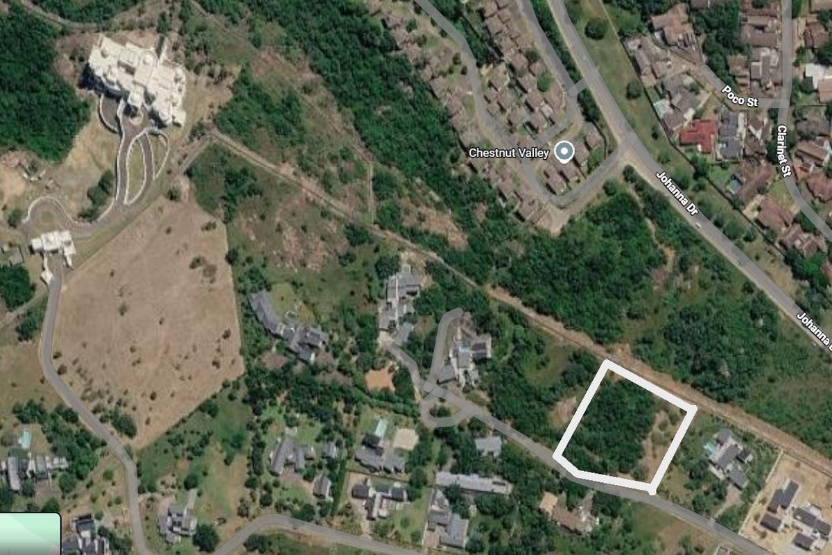 An aerial view of a vacant residential plot highlighted in white, situated within a developed suburban area with surrounding vegetation.