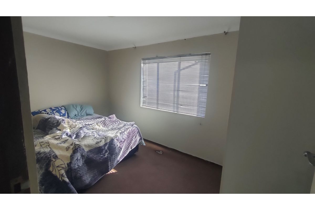 A bedroom featuring neutral wall tones, a window with fitted venetian blinds, and carpeted flooring.