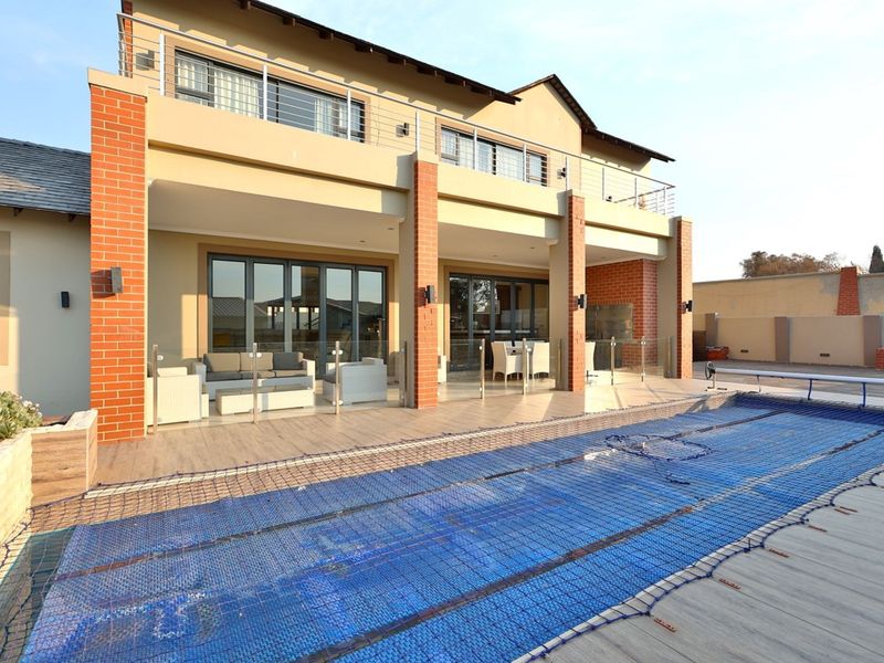Spacious rear patio area featuring a swimming pool with safety net, glass balustrades, and direct access to the home through large sliding glass doors.