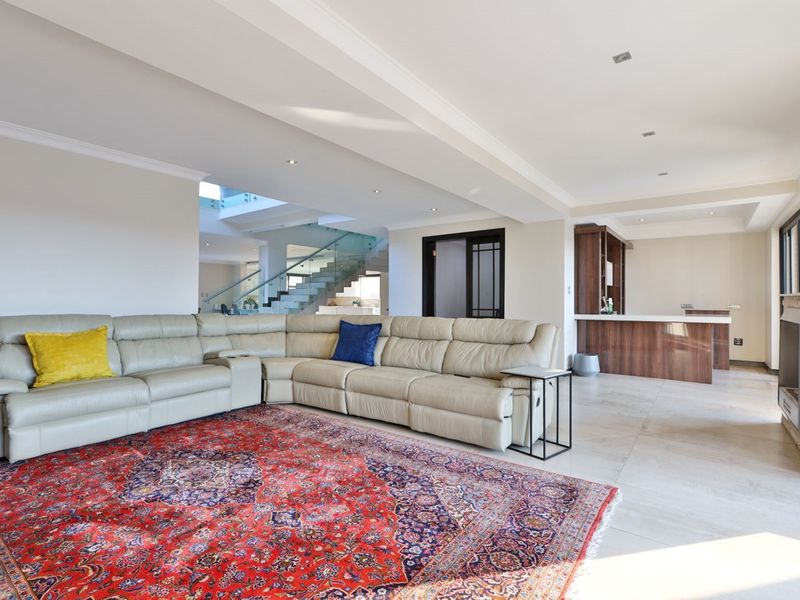 Spacious open-plan living area featuring a stone fireplace, built-in bar, and a modern staircase with glass balustrades, finished with neutral tiled flooring.