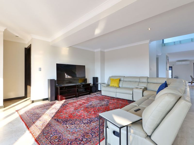 Spacious living room featuring neutral tiled flooring, recessed downlighting, and a modern open-plan layout with a glass balustrade staircase visible in the background.