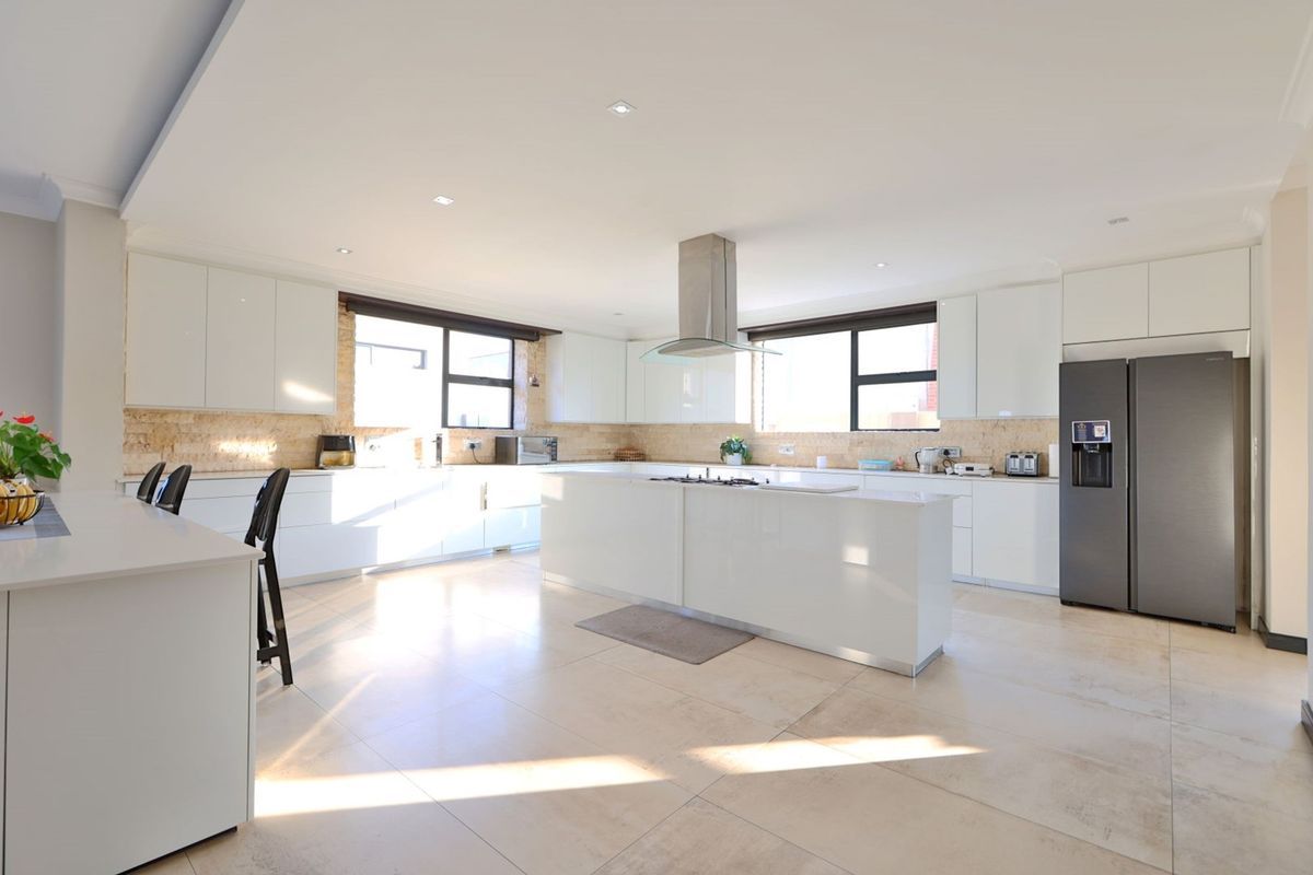 Modern, spacious kitchen featuring a large central island with a gas cooktop, sleek white cabinetry, stone countertops, and high-quality tiled flooring.